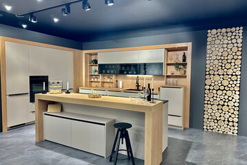 Moderne Inselküche mit Bar in Holzoptik, beigen Fronten und Hängevirtine  mit schwarzen Glaselementen von Küchen & Wohnwelt Holzinger.