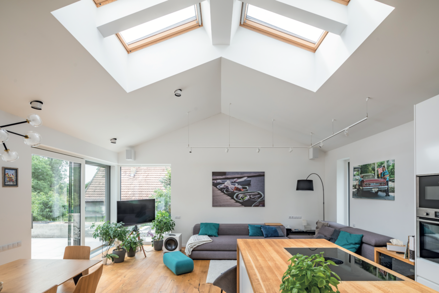Internorm zeigt einen Wohn-Essbereich mit einer grauen Couchlandschaft und weisser Küche mit Holzakzenten in einem Dach mit Fenstern in der Dachschräge.