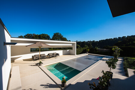 RUHA präsentiert eine Terrasse mit großen beigen Fliesen, einem Pool, einer Lounge und Bepflanzung.