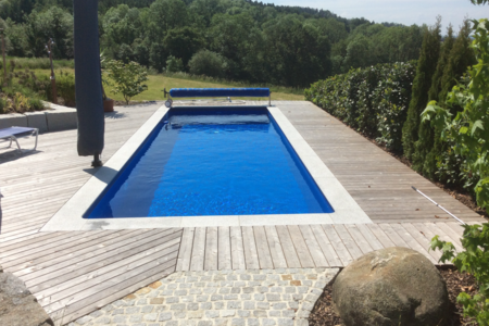 Gartenbau Schmid zeigt einen rechteckigen Pool mit Holzverbau rundeherum und verschiedene Hecken als Sichtschutz.