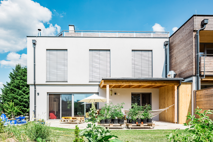 Capatect zeigt ein Einfamilienhaus mit einer überdachten Terrasse und Holzverkleidung , große Fenster mit Rollläden und einem modernen Flachdach.