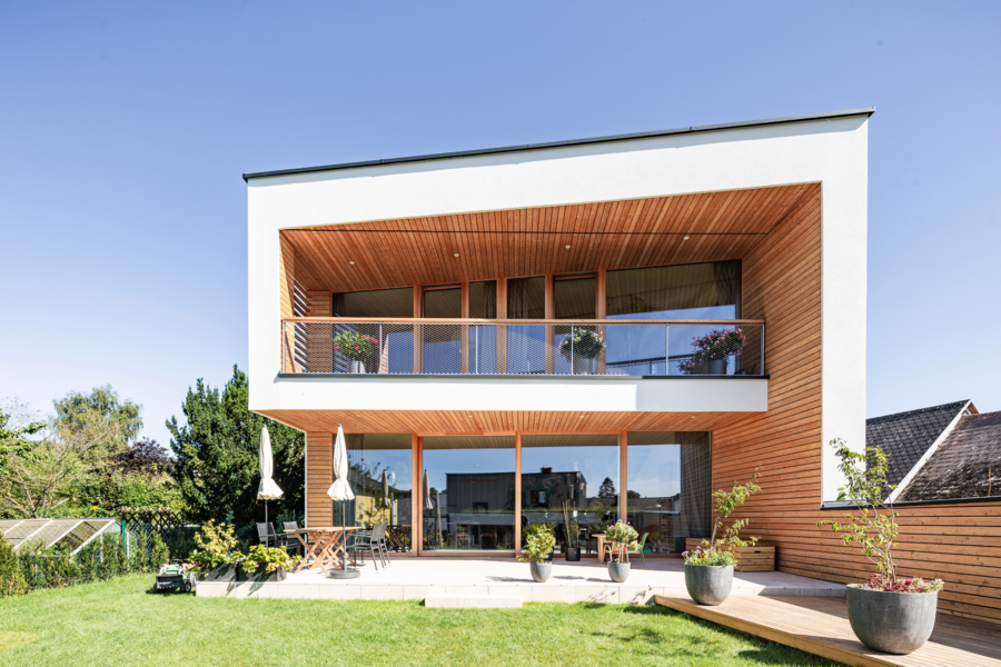 Modernes Einfamilienhaus mit Holzverkleidung und Schrägdach mit einer überdachten Terrasse, einer Sitzgruppe und Sonnenschirmen von Capatect.