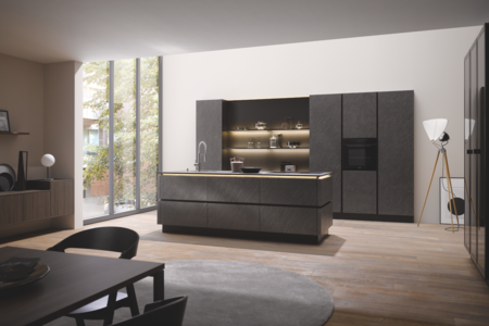 Tischlerei Bauer zeit eine moderne Küche mit Holzboden und einer Kücheninsel in dunklem grau mit Spülbecken und großem Einbauschrank mit integriertem Backofen von Häcker Küchen.