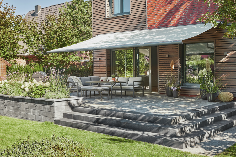 WAREMA präsentiert die Markise einer gemütlichen Terrasse mit Outdoor-Möbeln und einem Grill um Sonnenschutz zu spenden.