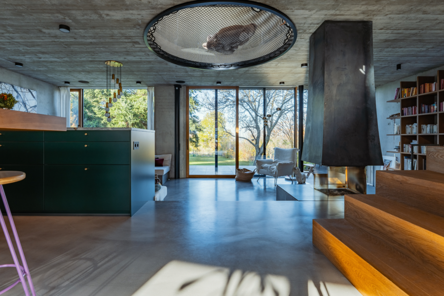 ARDEX zeigt ein Wohnzimmer mit einer Holztreppe, schwarzen Möbeln, grauem Boden und einem Kamin mit einer Schiebetür zur Terrasse von panDOMO.