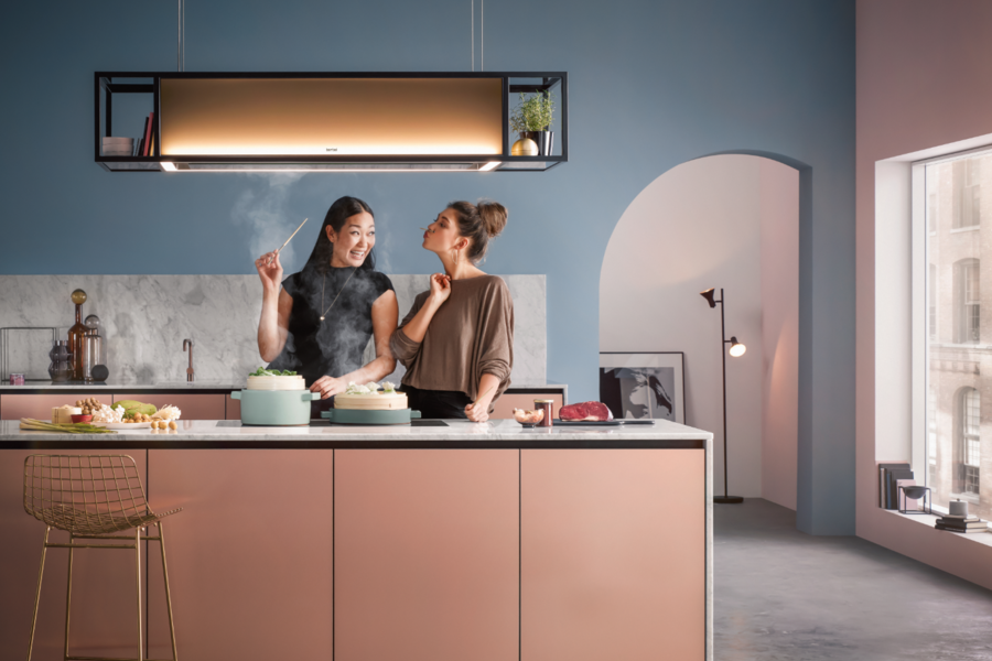 Zwei Frauen sind vergnügt beim Kochen in einer modernen Küche unter Verwendung eines beleuchteten berbel Dunstabzugs mit der Bezeichnung Deckenlifthaube Skyline Frame.