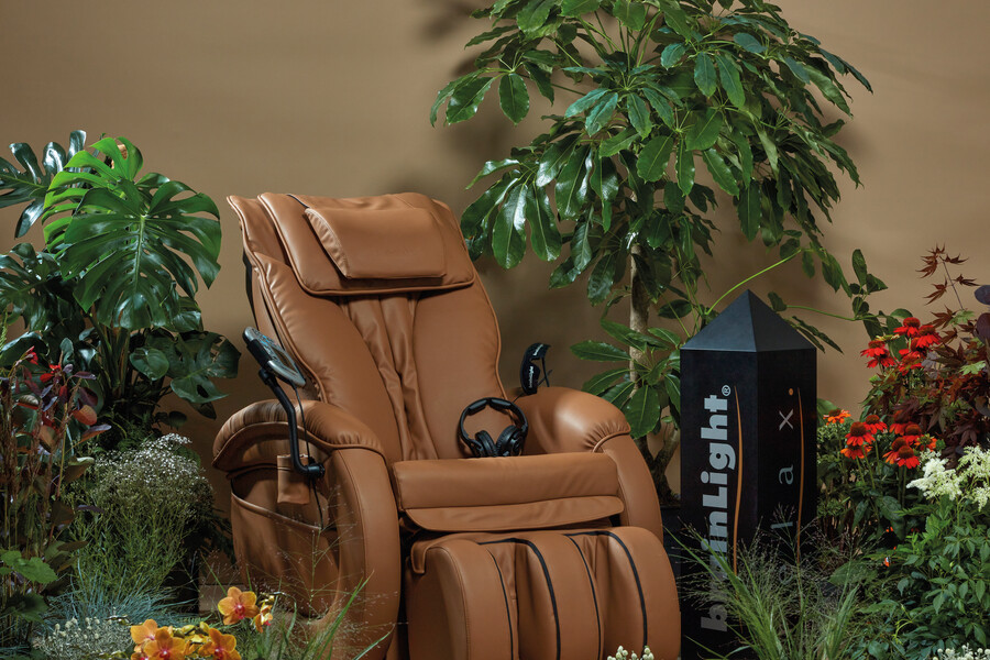 Der braune Massagestuhl mit mehreren Funktionen aus Leder von brainLight, in einer bepflanzten Wohlfühloase.