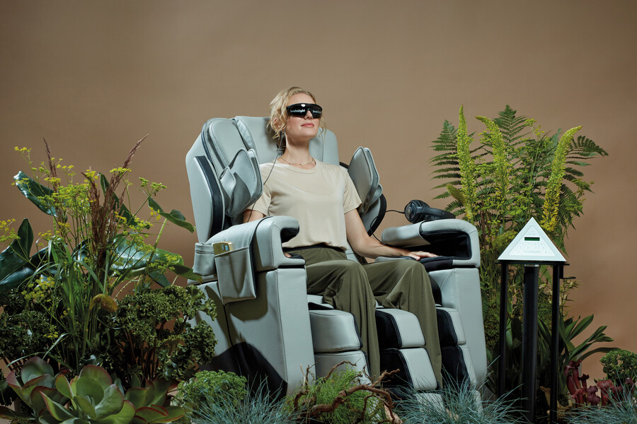 Eine junge Dame mit Brille, lässt sich von dem dunkelblauen Massagestuhl von brainLight, in einer bepflanzten Entspannungsoase massieren.