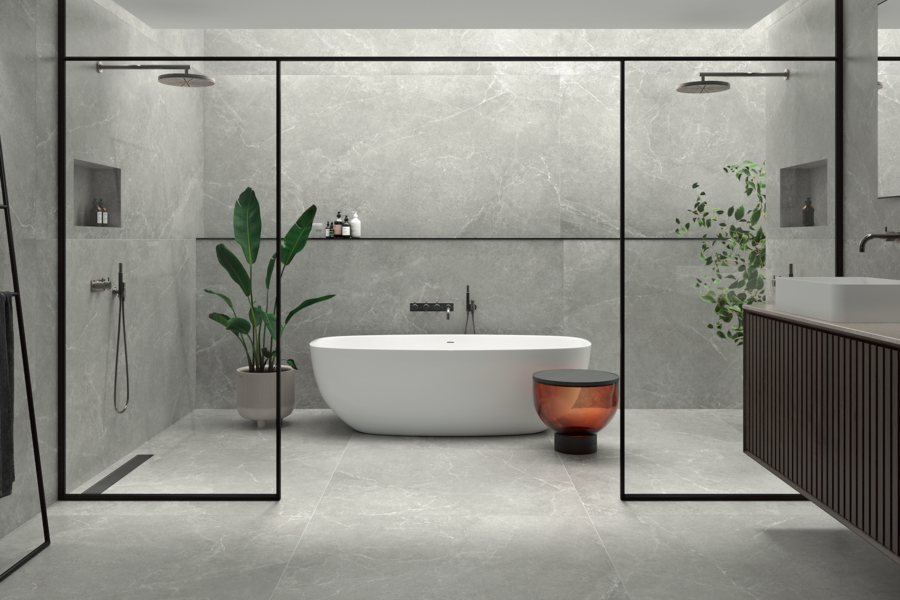 C. Bergmann zeigt ein offenes Badezimmer mit grauen Wandfliesen und Fliesenboden mit freistehender Badewanne und Dusche mit Glaswand und schwarzem Rahmen von Argenta.