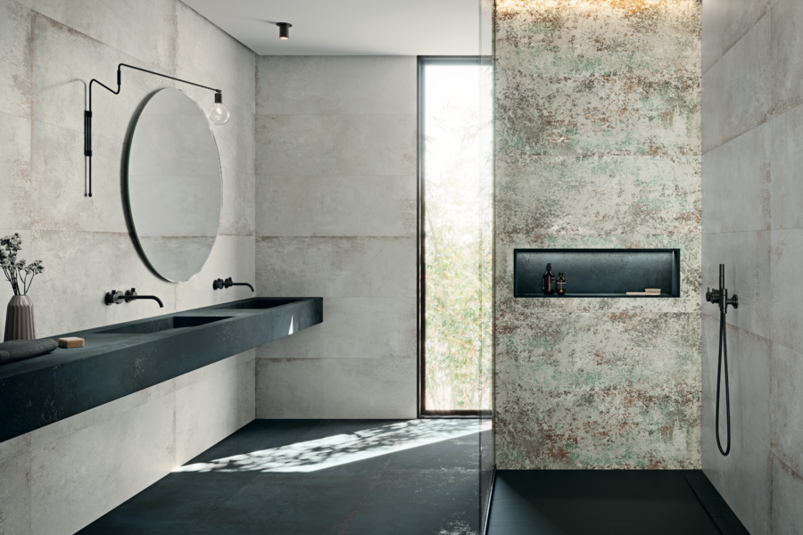 C. Bergmann zeigt ein Badezimmer mit schwarzem Fliesenboden und Doppelwaschtisch, einer offenen Dusche mit gemusterten Fliesen an der Wand und schwarzen Armaturen von Grespania.