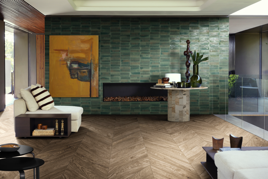 C. Bergmann zeigt ein Wohnzimmer mit Wandfliesen in verschiedenen Grüntönen, einem in der Wand verbauten Kamin und einem schönen Holzboden und gemütlichem Loungesessel von Marazzi.