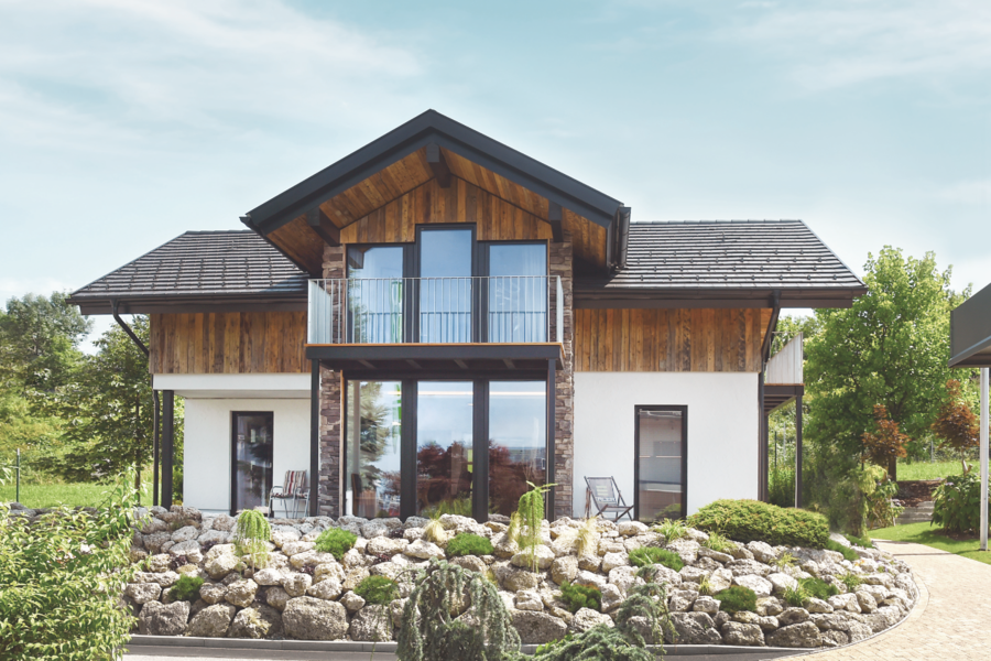 Ein schönes Einfamilienhaus mit Holzelementen und großem, überdachten Balkon mit Metallgeländer und einer Terrasse von ERLER BAU GmbH.