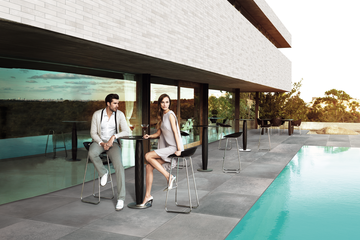 2 Personen sitzen vor einer puristischen Villa neben einem Pool.