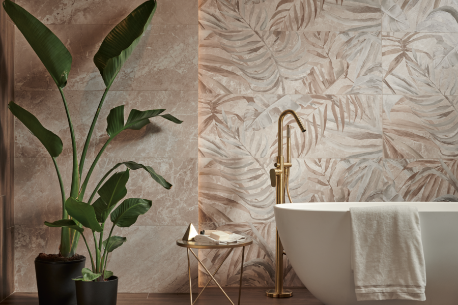 Felbermair zeigt ein Badezimmer in Naturtönen und einer freistehenden Badewanne mit goldenen Armaturen und gemusterten Wandfliesen mit Blättern und großen Pflanzen von Keraben.