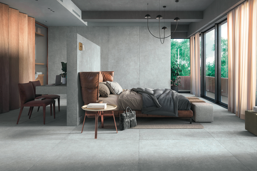 Felbermair zeigt eine Schlafzimmer mit grauem Fliesenboden und gefliester Wand, einem Doppelbett aus Leder und einer angrenzenden Trennwand mit Schminktisch und zwei braunen Stühlen von Mirage.