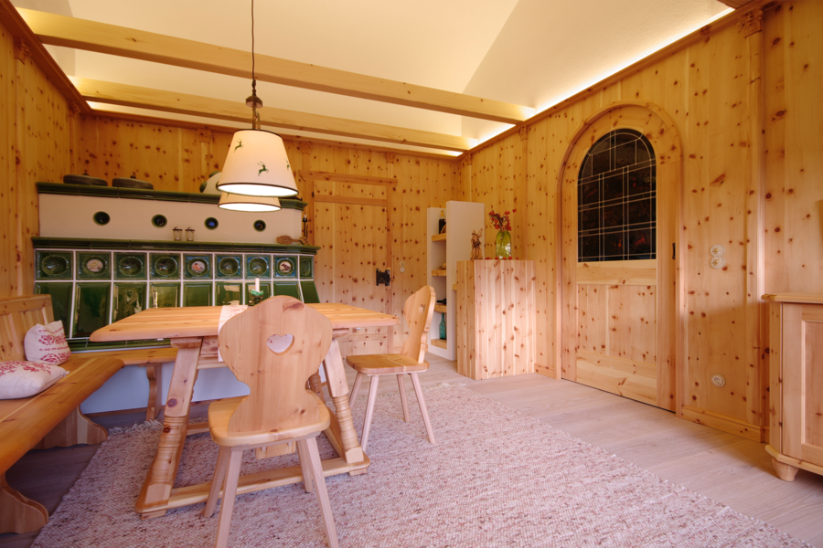 Traditionelle Zirbenstube mit Wandverkleidung, Kamin und Holzboden sowie passender Holztüre aus Zirbenholz - gefertigt von WOHNHAUS Grill & Ronacher.
