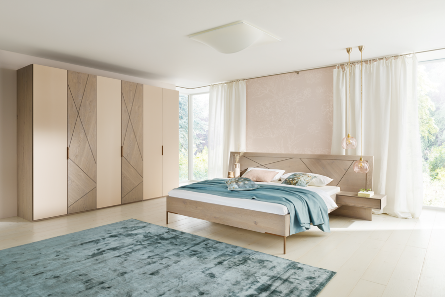 WOHNHAUS Grill & Ronacher zeigt ein modernes Schlafzimmer mit einem Doppelbett aus dem Holz der Asteiche mit grauen Einlegearbeiten und dazupassendem Kleiderschrank.