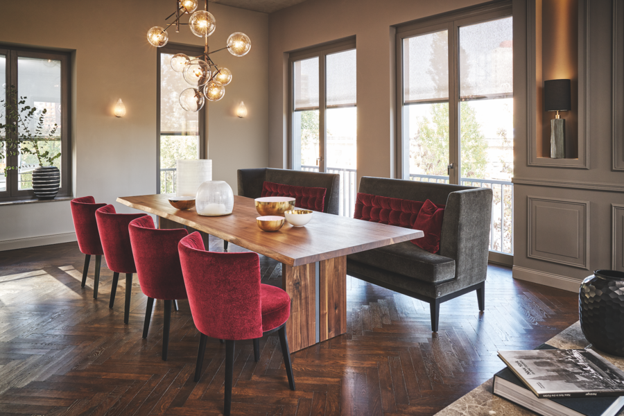 Grill & Ronacher zeigt eine lange Holztafel in einem sehr dunklen Esszimmer mit roten Stühlen, dunkelbraunem Fischgrätenboden und hohen Fenstern. von Bielefelder Werkstätten.