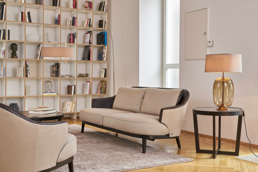 Grill & Ronacher zeigt einen klassisch, biege eingerichteten Raum mit bis zur Wand ragendem Bücherregal in gold, kleinem Sofa und Tischchen von Bielefelder Werkstätten.