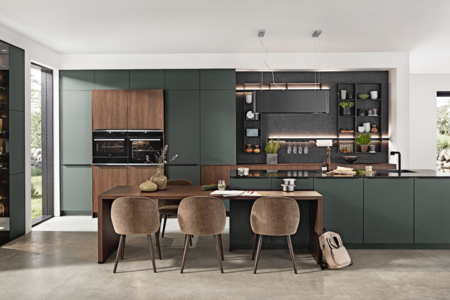 Grill & Ronacher zeigt eine Küche mit Esstisch integriert in einem dunklen olivegrün mit braunen Dekoartikeln und hellbraunen Stühlen von Nobilia.