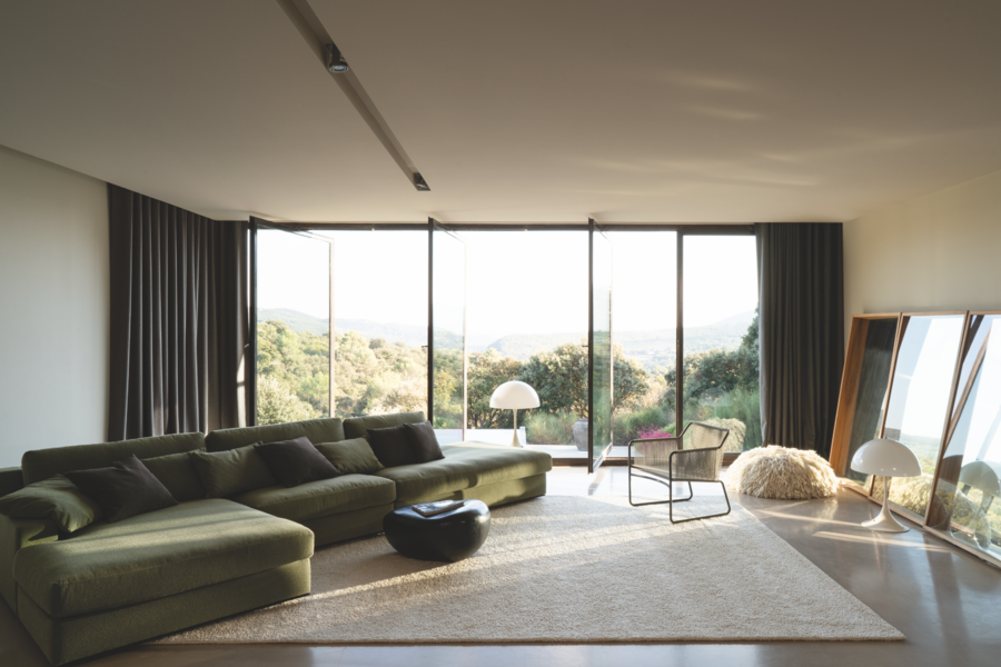 WOHNHAUS Grill & Ronacher präsentiert ein gemütliches Wohnzimmer mit grüner Couch und beigem Teppich mit Spiegelfront und Aussicht in den Garten von Bielefelder Werkstätten.