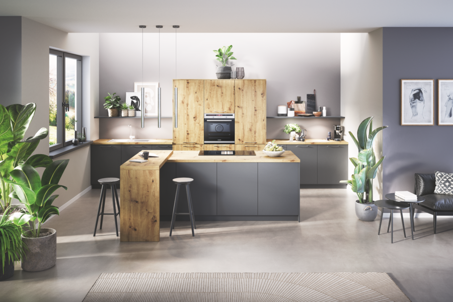 WOHNHAUS Grill & Ronacher zeigt eine Häcker Küche mit grauen Fronten, einem Schrank und Akzenten aus hellem Holz mit integrierter Bar und Hockern.