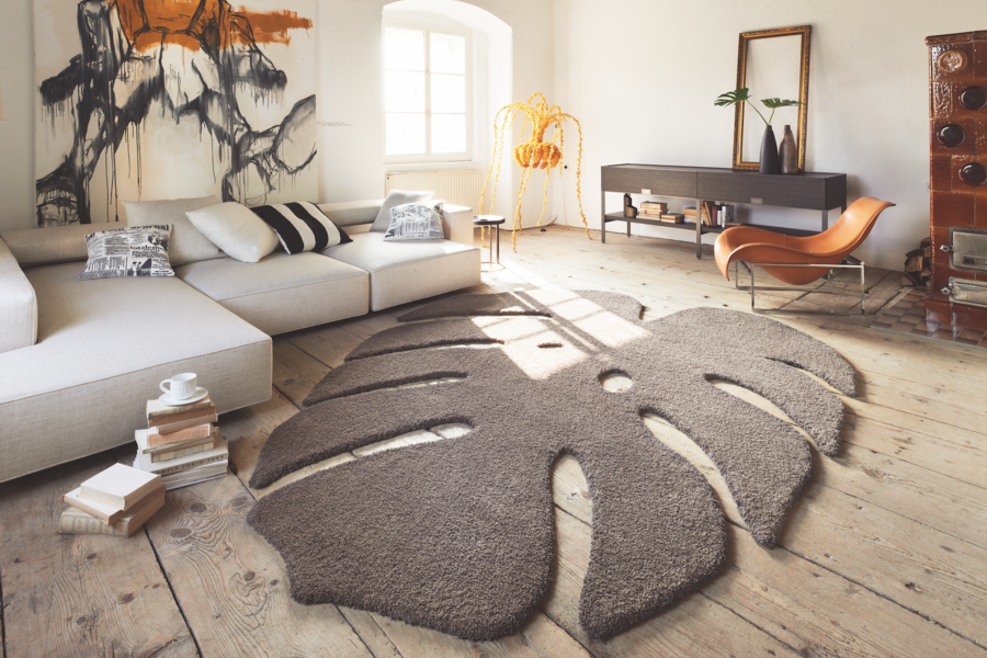 WOHNHAUS Grill & Ronacher zeigt ein modernes Wohnzimmer mit einem freiliegenden, braunen Teppich in der Form eines Blattes und einer hellen Couch von Landegger.