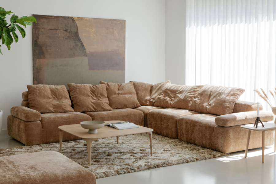 WOHNHAUS Grill & Ronacher zeigt ein Wohnzimmer in Brauntönen mit einer großen hellbraunen Couch, einem hochflorigen Teppich und Beistelltisch aus Holz von SITS.