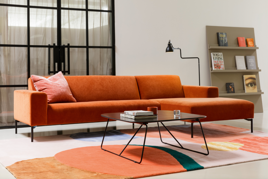 WOHNHAUS Grill & Ronacher zeigt ein modernes Wohnzimmer mit einer orangen Couch und einem Beistelltisch aus Holz auf einem gemusterten, freiliegenden Teppich von SITS.