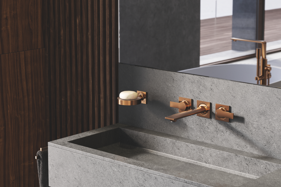Grohe zeigt ein Badezimmer mit Holzverkleidung an der Wand und Waschtisch aus Beton mit einer grauen Rückwand, eckigem Waschbecken und Armaturen in altgold.