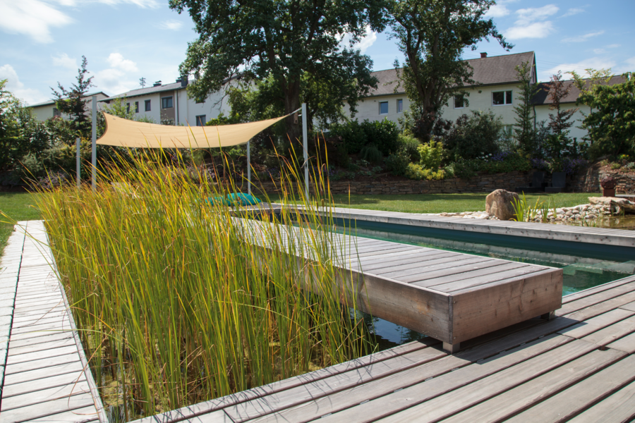 Ein Sonnensegel sorgt für effizienten Sonnenschutz am Pool mit Holzsteg von Hablesreiter.