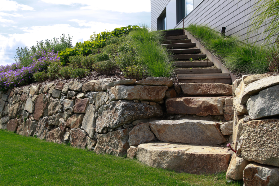 Hablesreiter zeigt eine Mauer aus Granitsteinen mit einer Holztreppe die in die zweite Etage des Gartens führt.