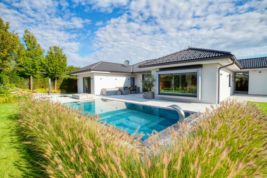 Hartl Haus zeigt einen weißen Bungalow mit schwarzem Walmdach und einem rechteckigen Pool auf der Terrasse.