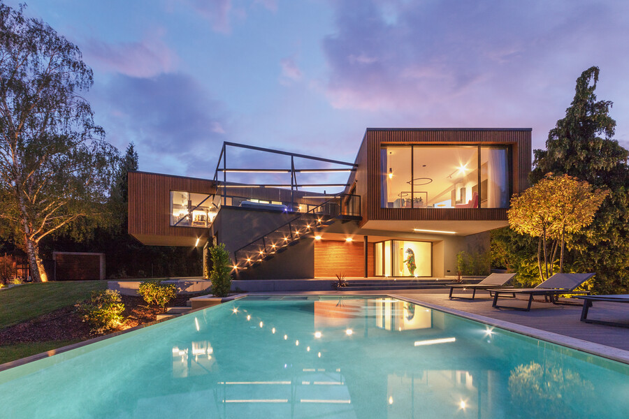 Internorm präsentiert ein modernes Haus mit einer Glasfront mit Blick, Richtung gepfelgter Außenanlage mit Pool.