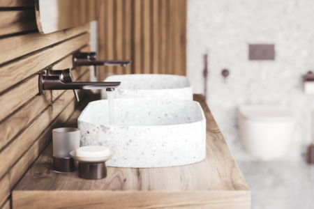 Jörger zeigt einen Doppelwaschtisch mit gesprenkeltem Waschbecken und Waschtisch aus Holz mit Armaturen, Mischbatterie und Halterungen in Nerz matt aus der Serie Exal.