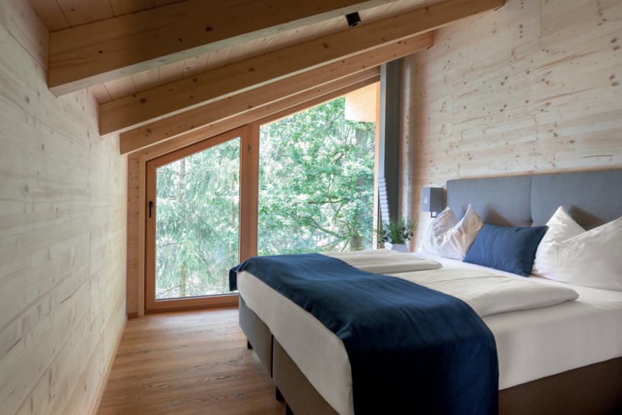 Schlafzimmer mit Wandverkleidung aus Holz und unter der Dachschräge großem Fenstern und einer Terrassentür von Josko.