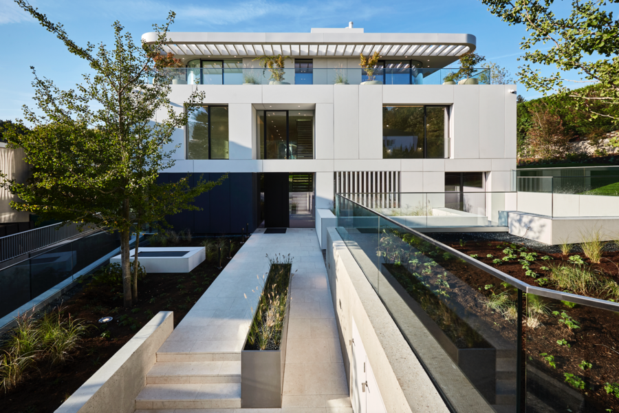 Josko zeigt den Zugang zu einem modernen Haus mit Flachdach und vielen Fenstern und einen minimalistisch bepflanzten Garten mit Glasgeländer neben dem Gehweg.