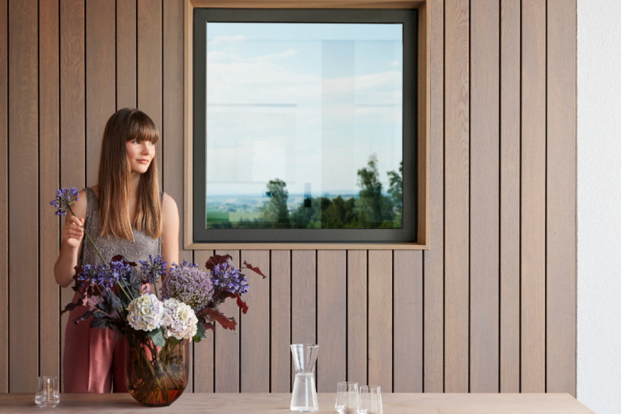 Frau mit Blumenstrauß vor Außenwand mit Holzvertäfelung und Josko-Fenster.