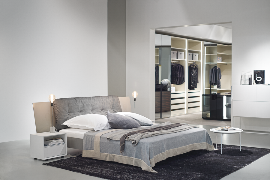 Kettnaker zeigt ein gepolstertes Bett in Grautönen sowie einen weißen Kleiderschrank im Hintergrund.