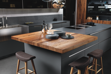 Einrichtung & Design Köck zeigt eine formschöne INTUO Inselküche mit edelstahl Griffmulden und aufgesetztem Bartisch.