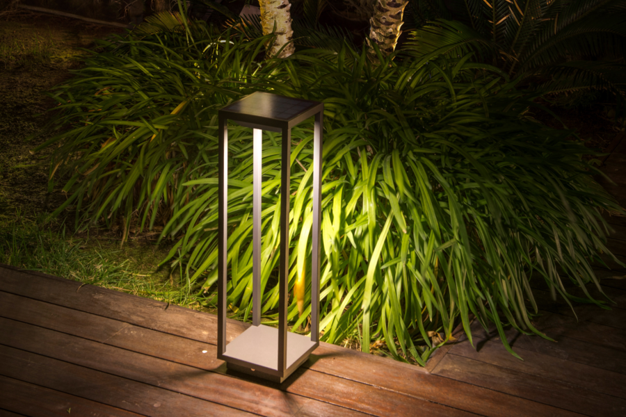 Lampenwelt präsentiert die neuen Solarlampen als Laterne auf dem Holzboden einer Terrasse mit Palmen im Hintergrund.