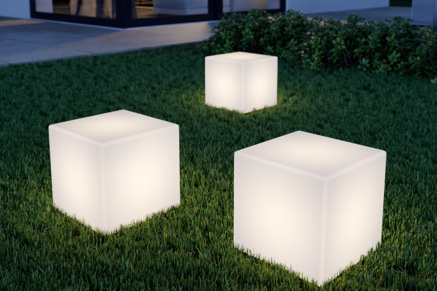 Lampenwelt präsentiert die neuen Solarlampen  als Leuchtwüfel im Gras liegend, im Garten  eines modernen Hauses.