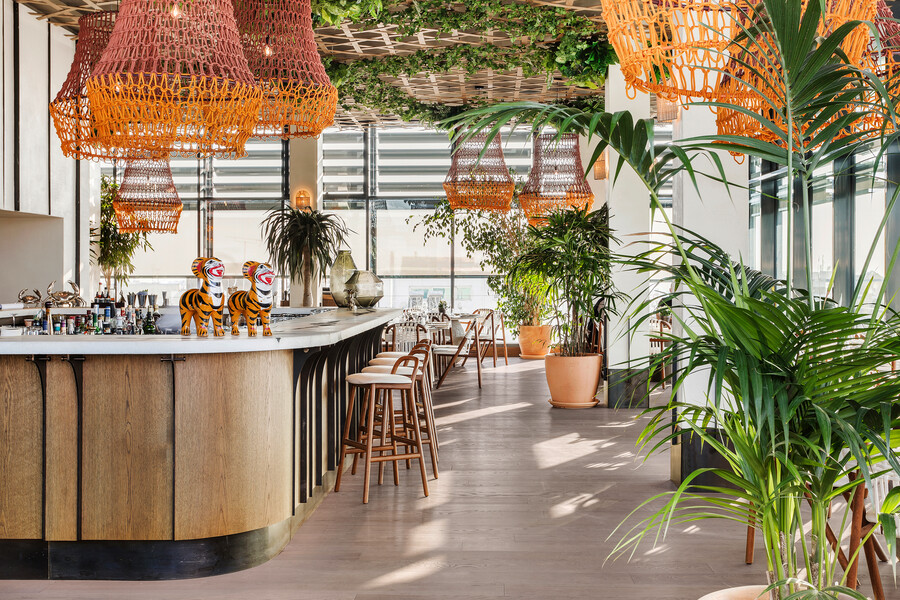 mafi © Margarita Nikitaki präsentiert Cor Esche in einer modernen Bar mit Urlaubsfeeling, Palmen, Statuen, orange gehalten, mit großen Fenstern.