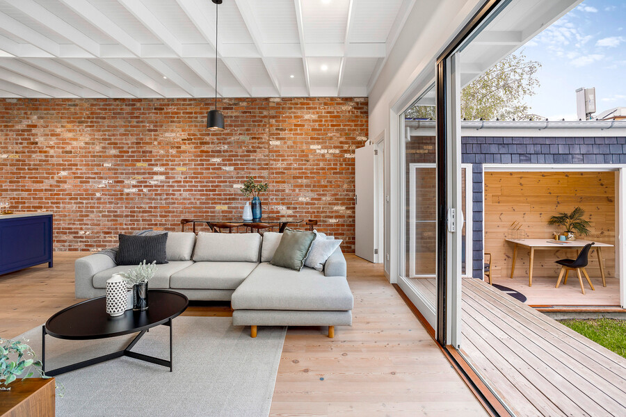 mafi präsentiert ein Wohnzimmer mit weiss geöltem Naturholzboden, weißer Decke und Rohbau-Look an den Wänden, einer grauen L-Couch und großer Glasschiebetür, welche direkt auf die Terrasse führt.