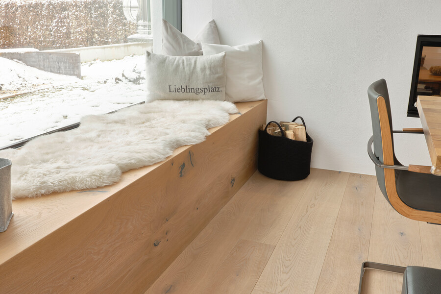 mafi präsentiert den weiß geölten Naturholzboden in form einer Sitzecke vor dem Fenster im Esszimmer mit weißem Fell und verschiedenen Kissen darauf liegend.