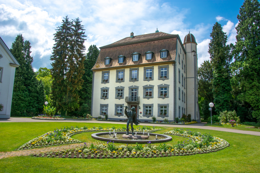Eine der Locations der Gartenlust-Veranstaltungsmärkte ist das Schloss Schönau, viele Fenster, hoher Turm, Vorgarten mit Brunnen, Statue.