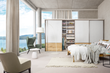 Mühleder Cabinet zeigt ein helles Schlafzimmer mit großflächigen Glaswänden, tollem Ausblick und einem Kleiderschrank mit Schiebetüren.