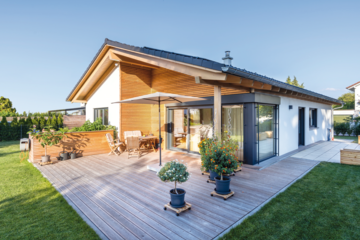 Regnauer zeigt einen modernen Bungalow mit Satteldach, Holzverbau, einer geräumigen Terrasse inklusive Outdoormöbeln und kleineren Pflanzen.