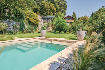 Friedrich Reitinger Schwimmbad und Wellness zeigt einen sehr natürlich gehaltenen Garten mit vielen Pflanzen und einem in den Boden eingelassenen, rechteckigen Pool mit Stufen und gefliester Umrandung.