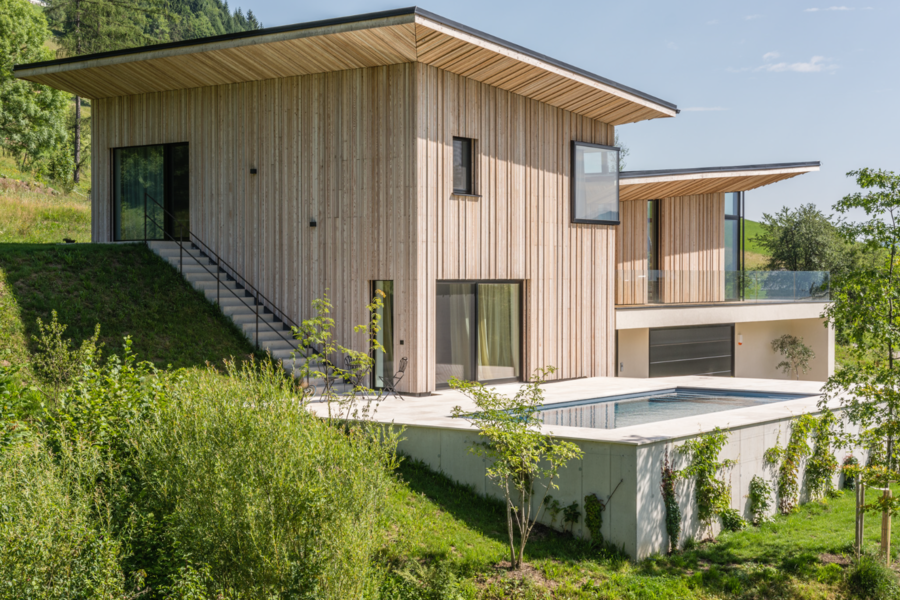 Silber Fenster zeigt ein modernes Architektenhaus in Hanglage mit teilweiser Holzfassade und Pool.